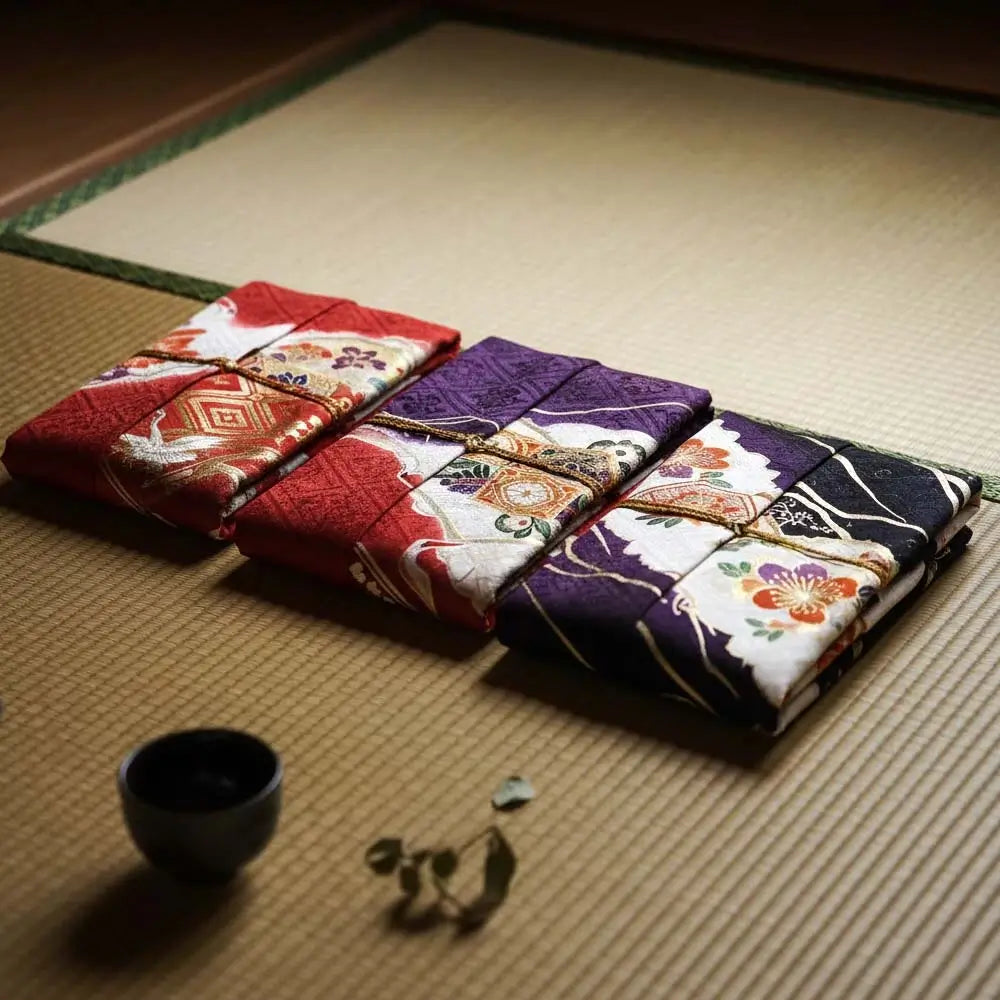 Trois kimonos japonais pliés aux couleurs rouge, violet et noir posés sur un tatami, illustrant la symbolique des couleurs dans la tradition japonaise.