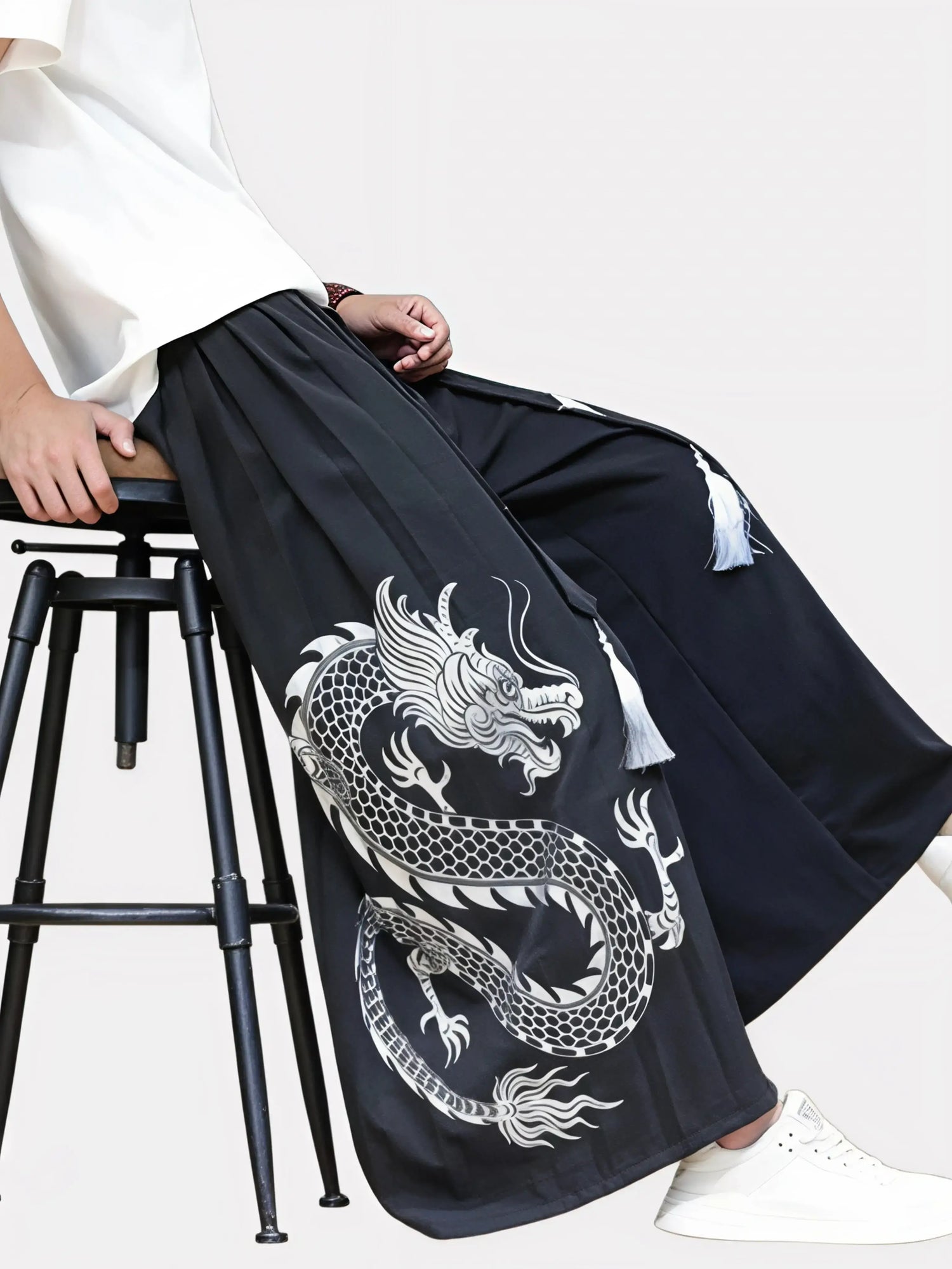 Homme assis portant un pantalon kimono noir à broderie dragon argentée, silhouette japonaise contemporaine et élégante.