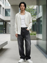 Pantalon baggy homme Kuro Classic noir, coupe large en denim effet légèrement usé, porté dans un environnement urbain chic avec chemise ouverte claire, débardeur blanc et sneakers blanches, style moderne et élégant.