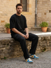 Homme assis en extérieur portant un pantalon japonais cargo en coton noir, coupe ample avec poches latérales.