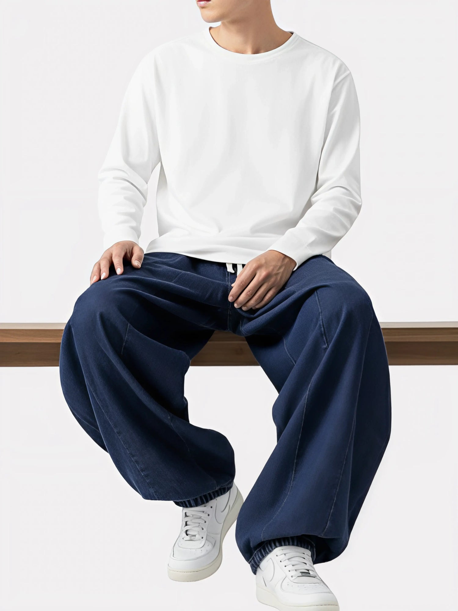 Homme assis portant le Jeans Sora bleu marine, pantalon kimono japonais ample et fluide, assorti Ă  un haut blanc minimaliste.