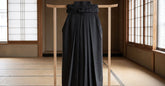 Hakama d'aïkido noir plissé présenté sur un support en bois dans un dojo clair