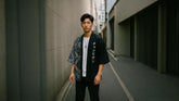 Homme asiatique moderne portant un kimono streetwear noir et gris à motif bandana, debout dans une ruelle japonaise minimaliste, style urbain chic avec t-shirt blanc et collier argenté.