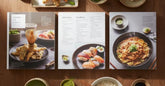 Livres de cuisine japonaise empiles avec des ingredients frais, matcha et baguettes sur une table en bois