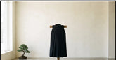 Pantalon hakama noir plissé présenté sur un support en bois dans une pièce claire