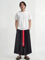 Pantalon hakama homme Kōsei noir, pantalon japonais traditionnel à plis larges avec ceinture rouge, porté avec t-shirt blanc et sandales, style minimaliste et élégant.