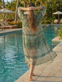 Vue dos du kimono de plage bohème Ocean Breeze, coupe longue fluide, tissu léger à motifs floraux verts et beiges, porté au bord d’une piscine tropicale