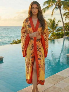 Kimono de plage long bohème orange et rouge Sun Flame, porté par une femme au bord d’une piscine tropicale, style estival chic et fluide