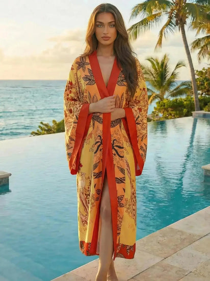 Kimono de plage long bohème orange et rouge Sun Flame, porté par une femme au bord d’une piscine tropicale, style estival chic et fluide