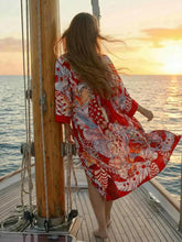 Vue de dos kimono rouge flottant au vent motif floral bohème sur un voilier au soleil couchant