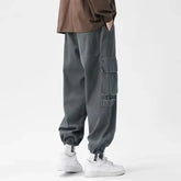 Pantalon cargo gris pour homme au style japonais, doté de grandes poches utilitaires et d’une coupe ample moderne avec chevilles élastiquées.