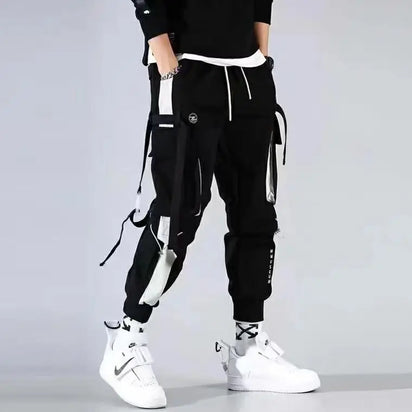 Homme portant le Pantalon Cargo Japonais Urban Street Tactical noir, coupe streetwear avec multi-poches et sangles décoratives.