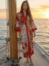Kimono long de plage bohème rouge Hana Fire porté par une femme sur un voilier au coucher de soleil – cover-up d'été élégant Kimono Nation