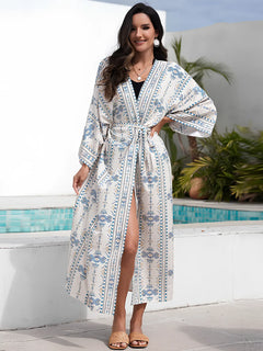 Kimono de plage long femme blanc à motifs géométriques bleus, ceinturé avec fente, porté au bord d’une piscine, style estival chic et élégant.