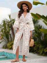 Kimono de plage long femme blanc et rouge à motifs bohèmes, porté ceinturé avec fente, chapeau de paille et sandales, style estival élégant au bord d’une piscine.