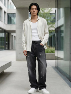 Pantalon baggy homme Kuro Classic noir, coupe large en denim effet légèrement usé, porté dans un environnement urbain chic avec chemise ouverte claire, débardeur blanc et sneakers blanches, style moderne et élégant.