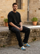 Homme assis en extérieur portant un pantalon japonais cargo en coton noir, coupe ample avec poches latérales.