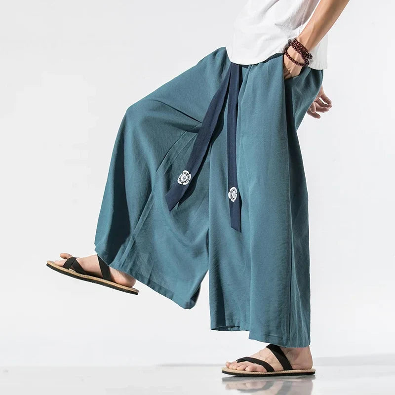 Homme portant un pantalon japonais ample bleu à ceinture ruban marine, style samouraï moderne inspiré du hakama traditionnel.