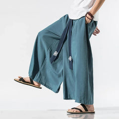 Homme portant un pantalon japonais ample bleu à ceinture ruban marine, style samouraï moderne inspiré du hakama traditionnel.