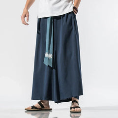 Homme debout portant un pantalon japonais bleu marine à ceinture contrastée vert foncé, coupe ample inspirée du hakama traditionnel samouraï.