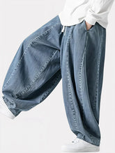 Pantalon japonais en jean pour homme vu de profil, denim bleu délavé, coupe ample et fluide, plis structurés le long de la jambe, taille ajustable avec cordon, style minimaliste inspiré du Japon.