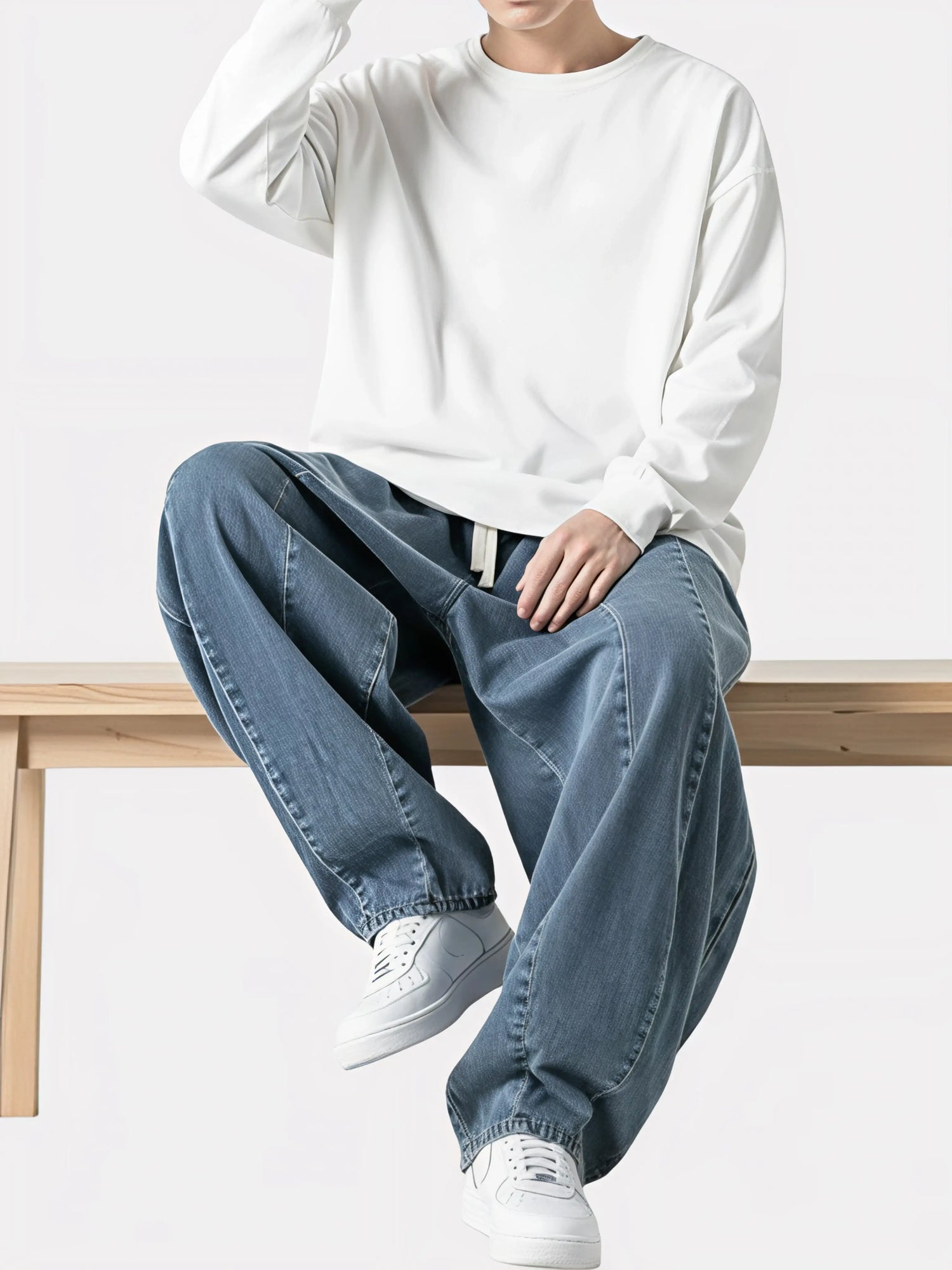 Modèle assis sur un banc en bois portant le Jeans Sora, pantalon kimono japonais ample en jean bleu clair avec cordon blanc et coupe oversize.