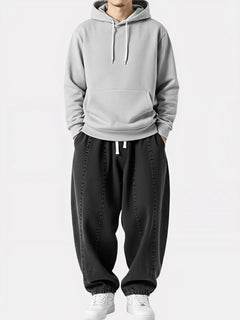 Homme debout portant le Jeans Sora noir, pantalon kimono japonais ample avec cordon blanc, coupe fluide et allure urbaine épurée.